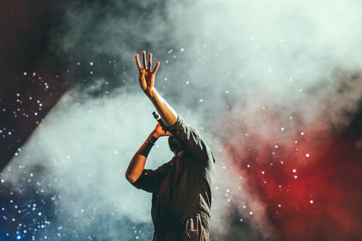 A crowd under stage smoke, one hand raised